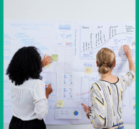 Two women at a whiteboard planning marekting
