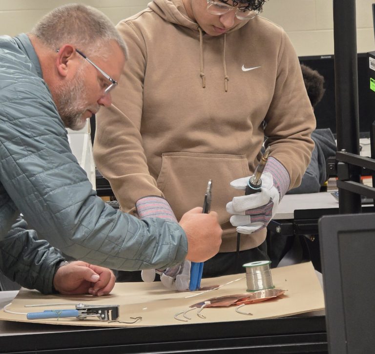 Factory worker showing student about sodering.